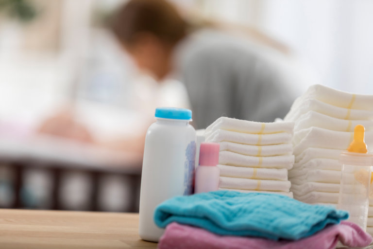 Close up of baby products sitting on a table in a baby's nursery. A mom is changing a baby's diaper in the background.