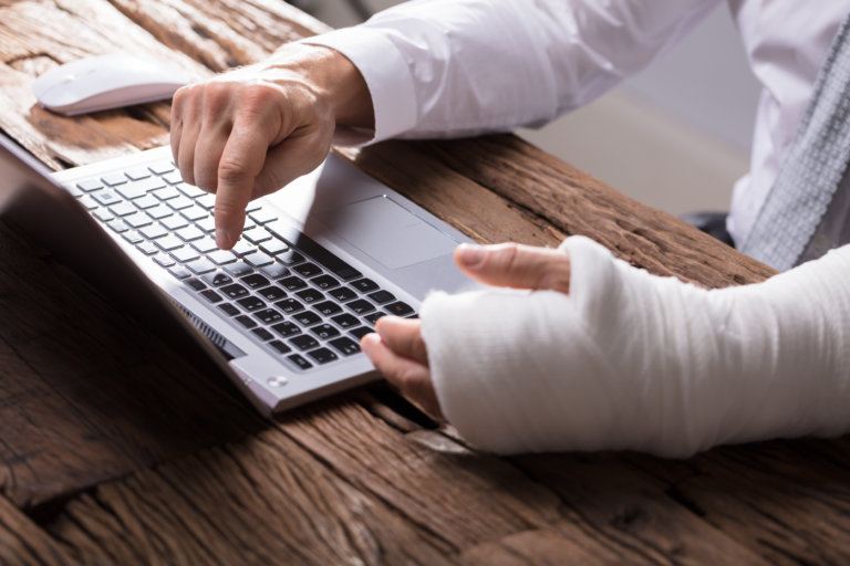 Close-up Of A Businessperson's Hand With Hand Injury Using Laptop