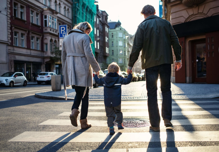 Parents helping child walk across the street.