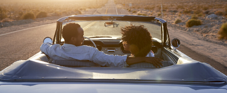 a man and a woman in a convertible driving down an empty road smiling at each other cause of car accidents