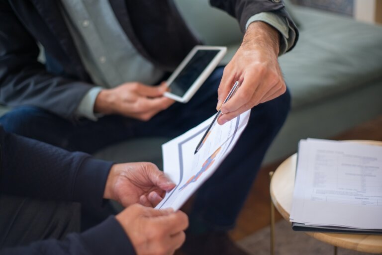 Two hands holding an insurance document, with one hand using a pen to point at the paper.