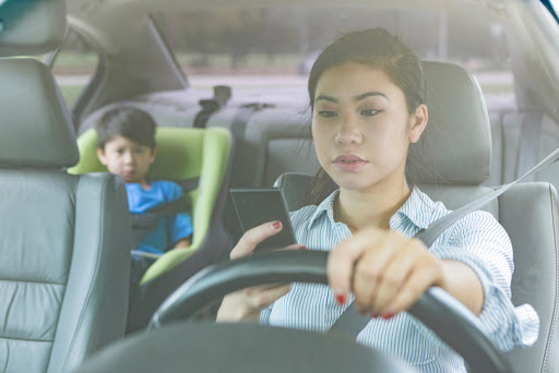 Mother texting and driving with her young child in the backseat.