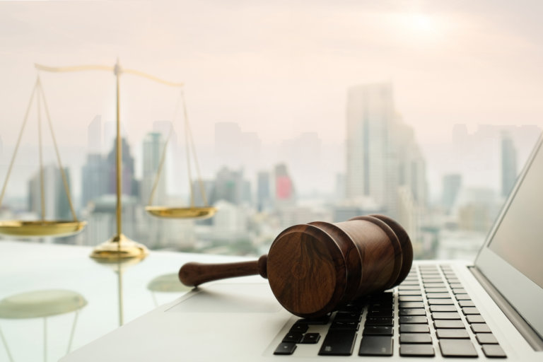 law legal technology concept. Wooden gavel on laptop keyboard with scales of justice in business city background.