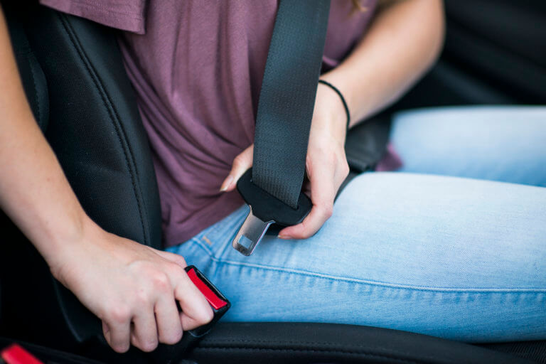 Close up of young female reaching over to put on a seat belt, practicing good safety habits.