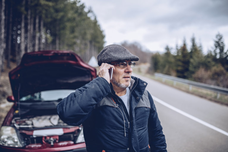 One man, mature man having car problems on the road in the mountains, talking on mobile phone.