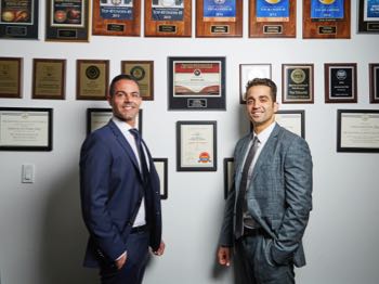 Jason B. Javaheri and Yosi Yahoudai in front of wall of awards