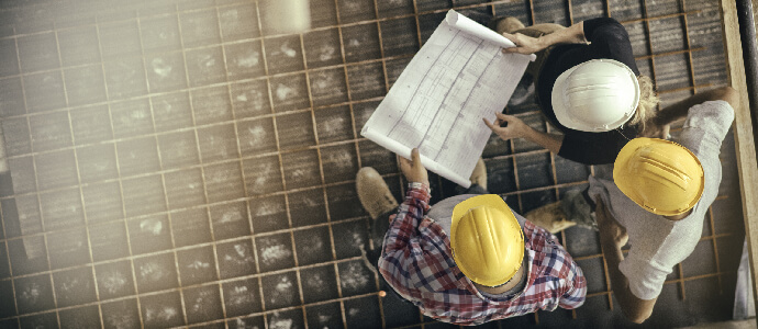 High angle view of three people with helmets, female architect, foreman and engineer on a construction site, looking down on a blueprint, copy space, supervisor negligence