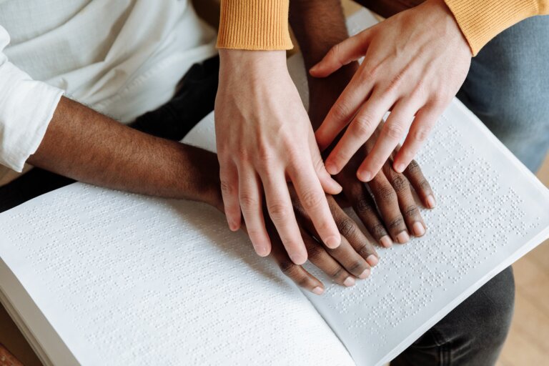 One spouse's hands helps the other's feel the braille script in a book.