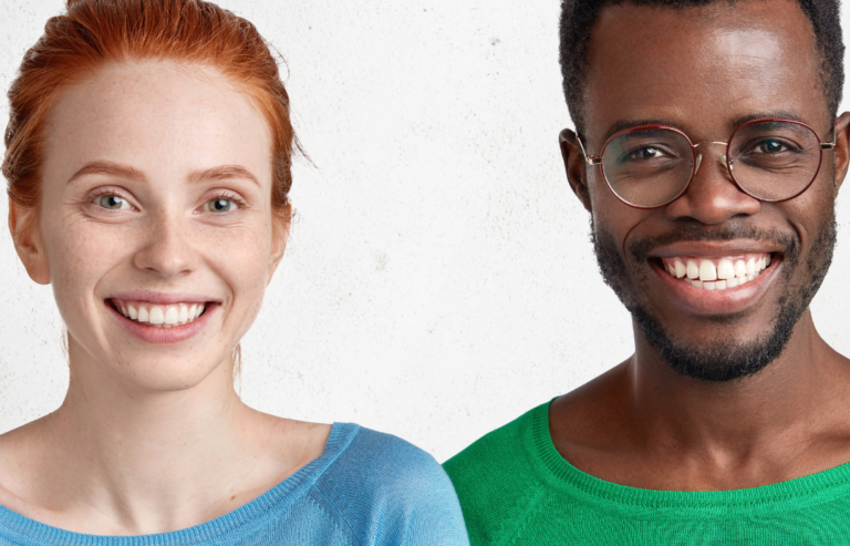young white woman with red hair wearing a blue shirt standing next to a young black man with short hair and glasses wearing a green shirt smiling