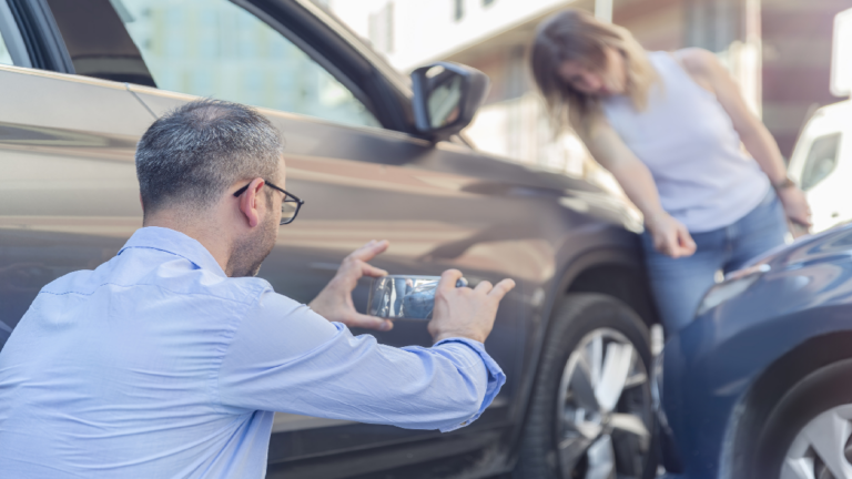 A man taking pictures of car damage after an accident