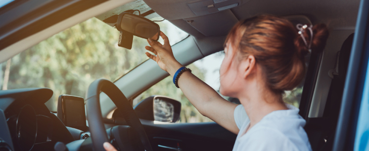 Teenage driver adjusting her mirror in car