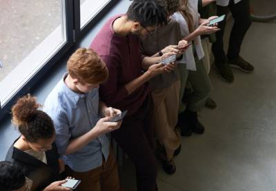 a group of teenagers standing in a hallway looking down at their cellphone screens
