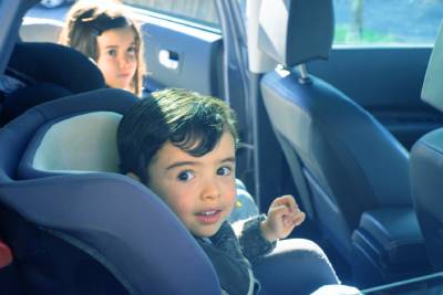 two young children in car seats inside a car looking at the camera