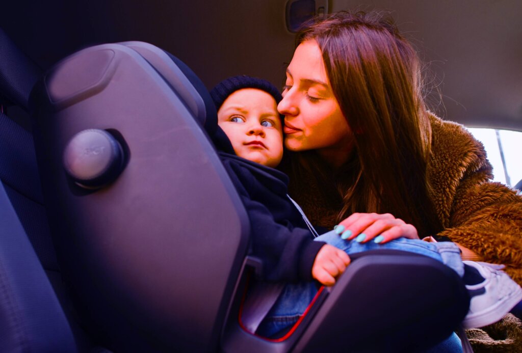 a mother kissing her young son as she puts him into a car seat