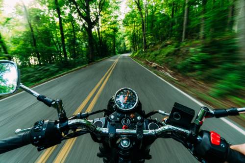 Motorradfahrer fährt mit hoher Geschwindigkeit eine bewaldete Straße entlang