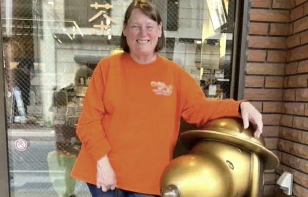 a woman in an orange shirt with her arm resting on a golden statue of Snoopy