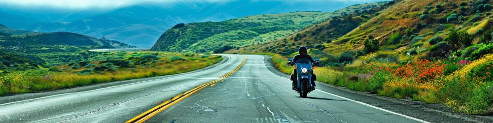 a motorcycle driving down an empty california highway during the spring time