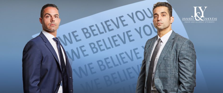 Jason Javaheri and Yosi Yahoudai, personal injury attorneys in California  at J&Y Law firm standing opposite one another with a sign that reads 'We Believe You, We Believe You, We Believe You' behind them.